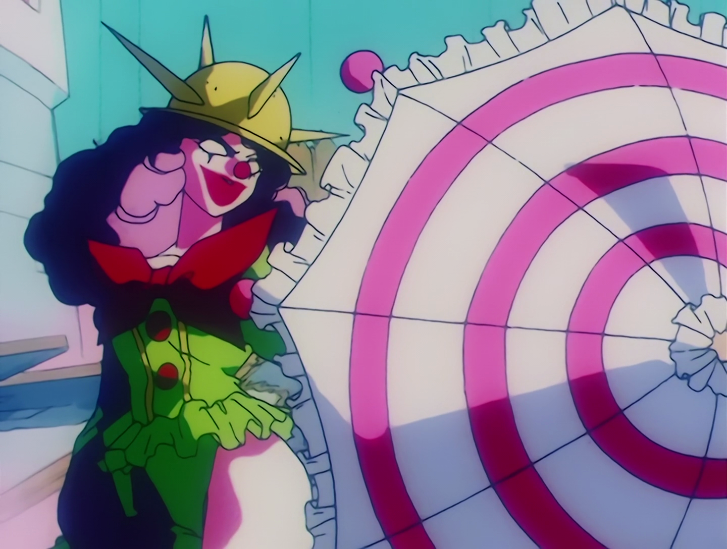 Bipierrot, a Cardian from Sailor Moon episode 56. She has clown makeup and curly pink hair under a spiked yellow hat. Her outfit is green and ruffled with a large red bow, and she’s holding a white umbrella with a pink swirl pattern.